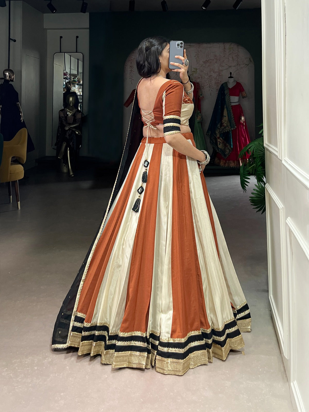 Woman taking a mirror selfie wearing a traditional outfit with orange, white, and black patterns.