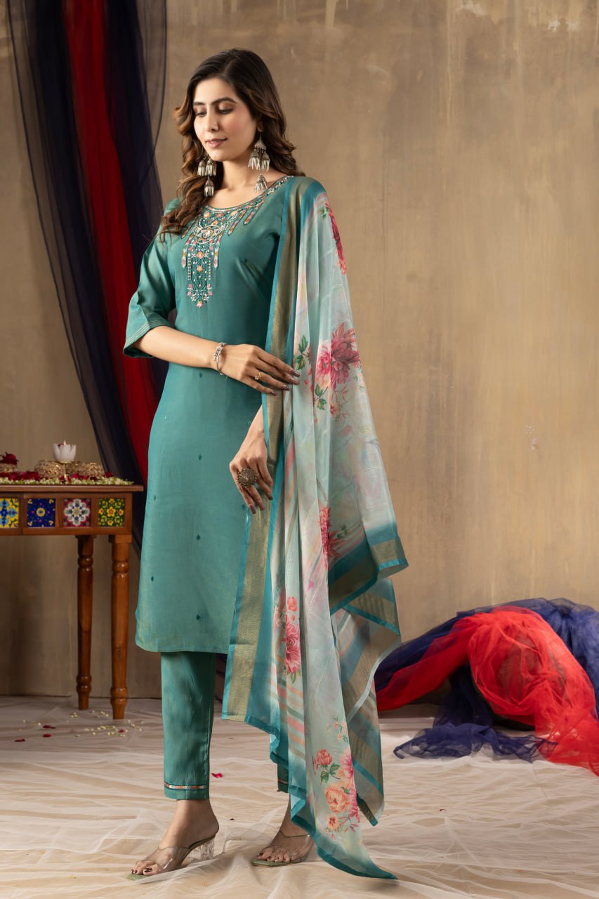 Woman in teal traditional outfit with floral dupatta against a neutral background