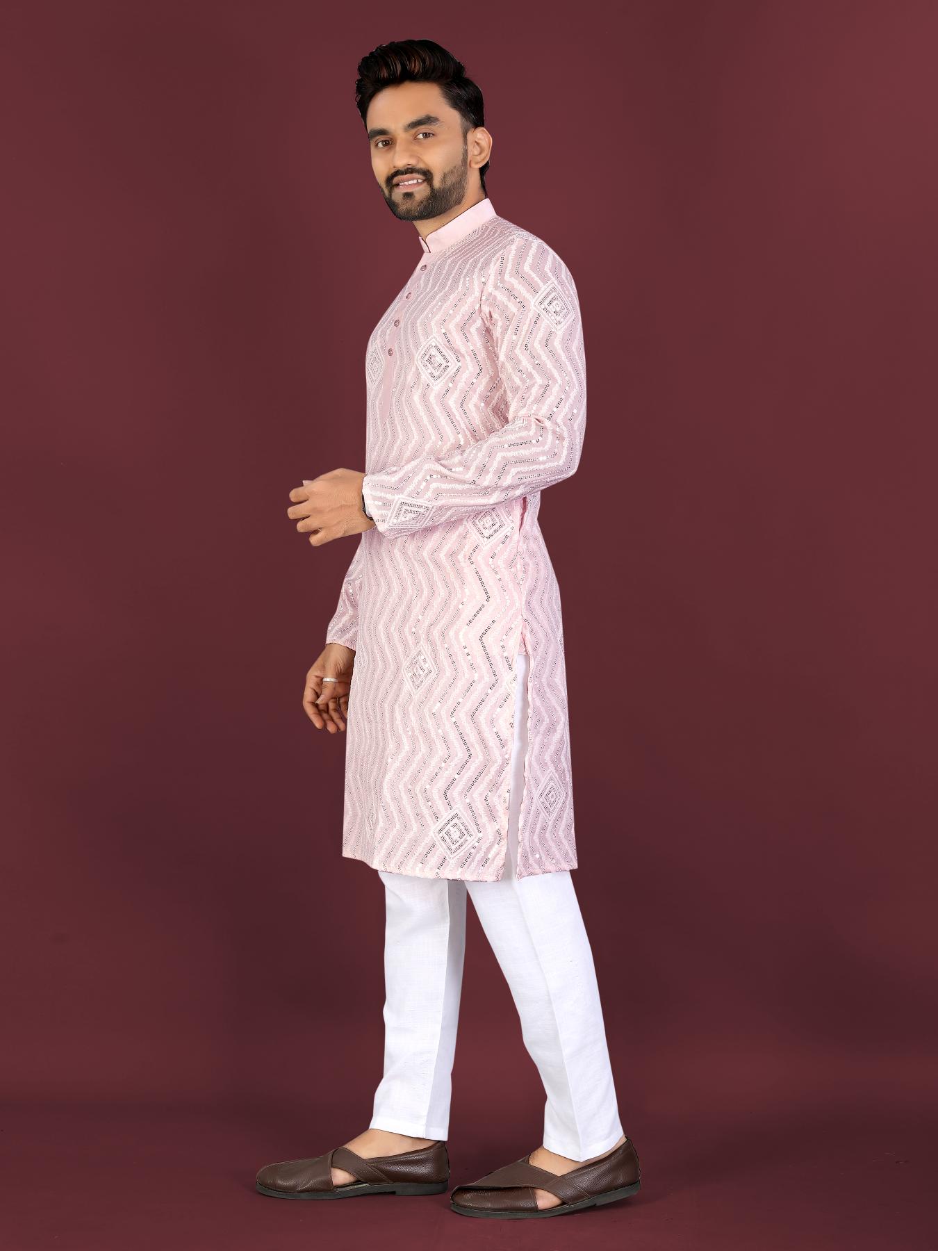 Man wearing a light pink embroidered kurta with white pants on a maroon background