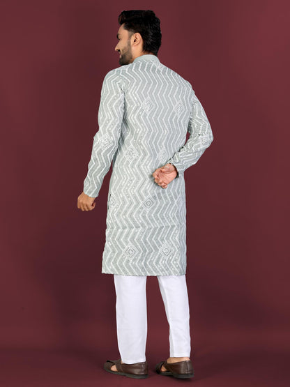Man wearing a light green embroidered kurta with white pants on a maroon background